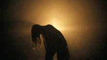 a silhouette of a woman in a dark room with the sun in the background