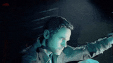 a man is standing in a dark room with a blue light shining on his face .
