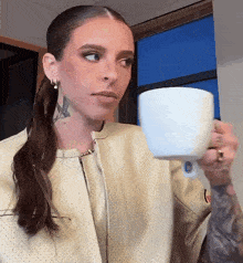 a woman with a tattoo on her arm is holding a white cup of coffee