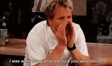 a man sitting at a table covering his face with his hands and says i was wondering what the fuck you were doing
