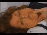 a close up of a woman 's face with her eyes closed and a man 's hand on her face .