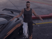a man in a black tank top stands in front of a silver car