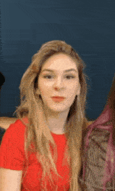 a woman with long blonde hair wearing a red shirt is looking at the camera .