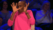 a man in a pink sweater is covering his face with his hands