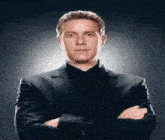 a man in a suit with his arms crossed looks at the camera