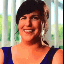 a woman in a blue top is smiling and looking at the camera .