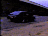 a black car is driving down a street in front of a building with a blue sky in the background