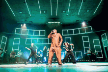 a man in a suit sings into a microphone while a group of people dance around him