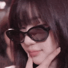 a close up of a woman wearing sunglasses and holding her hand to her face .