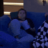 a woman sitting on a blue couch eating popcorn with a bucket that has the number 2 on it