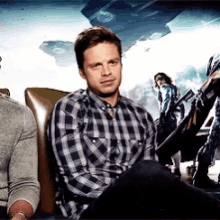 a man in a plaid shirt is sitting in a chair with two other men .