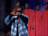 a man wearing sunglasses is singing into a microphone in front of a group of men in red robes