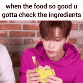 a young man in a purple hoodie is eating a sandwich and checking the ingredients .