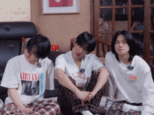 three young men are sitting in a living room with one wearing a nirvana t-shirt