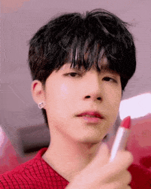 a young man is holding a lipstick in his hand and applying it to his lips .