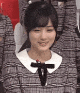 a woman in a plaid dress with a bow on her neck is sitting in a chair .