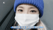 a woman wearing a blue beanie and a white face mask says " 카메라 에 "