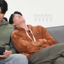 a man is laying on a couch with his head on another man 's lap .