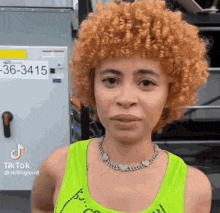 a woman with red curly hair is wearing a neon green tank top and necklace .