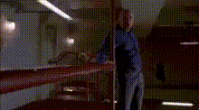 a man in a blue shirt is standing in a dark room behind a glass wall .