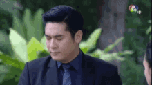 a man in a suit and tie is standing in front of a green bush .