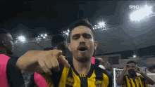 a man in a yellow and black striped jersey points at the camera
