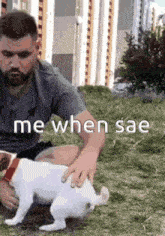 a man is petting a small white dog while sitting on the ground .
