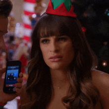 a woman wearing an elf hat is holding a cell phone with a screen that says samantha on it
