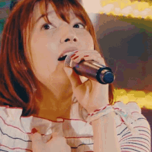 a woman is singing into a microphone with a striped shirt on