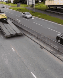 a white car is driving down a road next to a yellow car on a flatbed truck