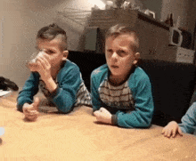 two boys are sitting at a table drinking water