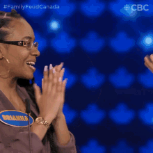 a woman wearing glasses and hoop earrings is clapping her hands in front of a microphone