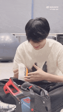 a young man is sitting on the floor holding a bag that says archer on it