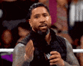 a wrestler is talking into a microphone while wearing a black vest