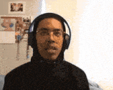 a young man wearing headphones and a black hoodie looks at the camera