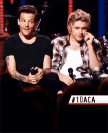 two men are sitting next to each other with a sign that says # 10aca on it