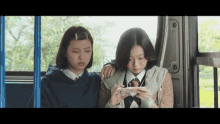 two girls sitting on a bus looking at a phone