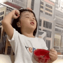 a little girl is holding a bowl of food and a spoon .
