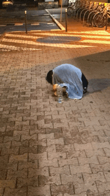 a person is kneeling down on a sidewalk with a bottle of water