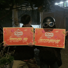 two people are holding up signs that say top 2 booyah