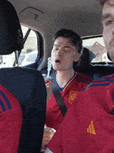 a man in a red adidas shirt sits in a car