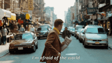 a man walking down a street with the words " i 'm afraid of the world "