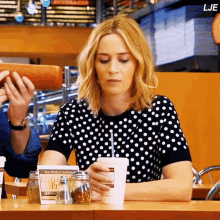 a woman in a black and white polka dot shirt is sitting at a table with a cup of coffee