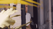 a woman in a white shirt is standing in a doorway with a plant in the foreground