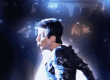 a man in a black shirt is dancing in a dark room with blue lights behind him .