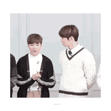 two young men are standing next to each other in front of a white wall .