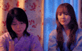 two young women are sitting next to each other in front of a window .