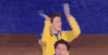 a man in a yellow jacket is dancing with his arms outstretched in front of a green background .