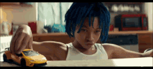 a young boy with blue hair is playing with a toy car on a table .
