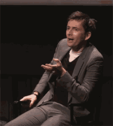 a man in a suit is sitting on a chair with his legs crossed and his hands on his hips .
